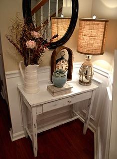 a white table topped with a mirror next to a lamp and vase filled with flowers