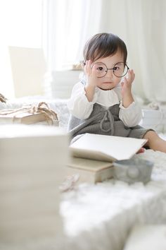 a small child wearing glasses sitting on a bed with an open book in front of her