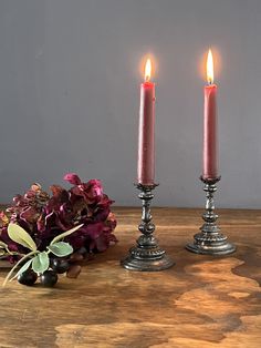 two candles are sitting on a table next to some purple flowers and greenery with berries