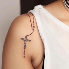 a woman wearing a white shirt with a cross tattoo on her arm and a rosary attached to the shoulder