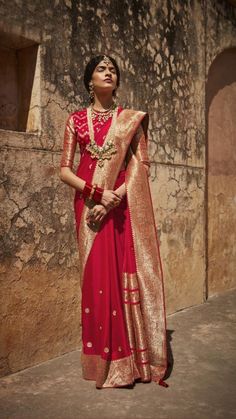 a woman wearing a red and gold sari standing in front of a stone wall