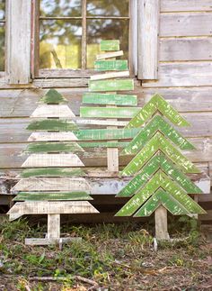 three wooden christmas trees sitting in front of a window on the ground next to grass