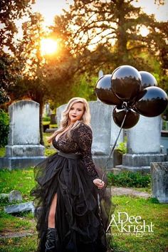 a woman in a long black dress holding balloons and posing for the camera at sunset