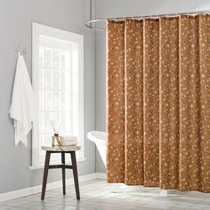 a bath room with a shower curtain next to a tub and a chair in front of a window