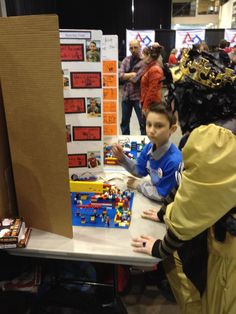 two children are playing with legos at a table in a store while adults look on