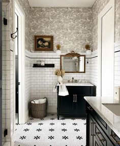 a bathroom with black and white tile flooring and wallpaper, along with a large mirror above the sink