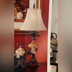 two lamps are sitting on a table in front of a red wall and framed painting