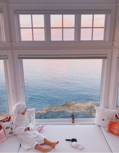 a person in a bathrobe sitting on a bed looking out at the ocean