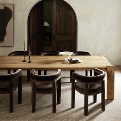 a wooden table surrounded by brown leather chairs in a room with an arched doorway and artwork on the wall