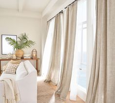 a living room with white furniture and curtains on the windowsills, along with a potted plant