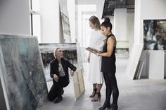 three women looking at art on display in an art gallery, one holding a book