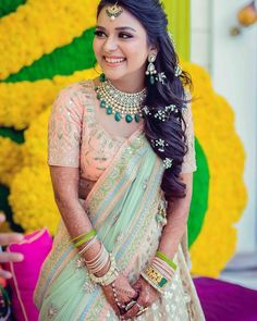 a woman in a green and white sari with jewelry on her neck, standing next to yellow flowers