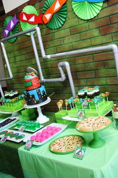 a table topped with cakes and desserts next to a brick wall covered in paper fans