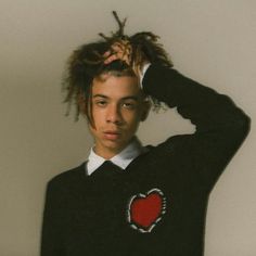 a young man with dreadlocks wearing a black sweater and holding his hair in the air