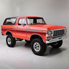 an orange pick up truck parked on top of a white floor next to a gray wall