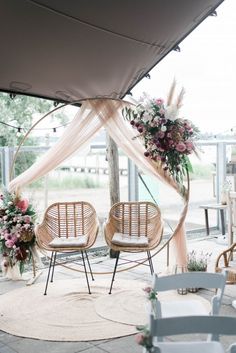 two chairs sitting under a canopy with flowers on it and one chair in the foreground