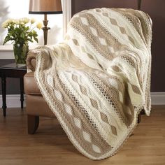 a chair with a blanket on top of it next to a lamp and flower vase