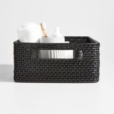 a black basket with white towels and toothbrushes in it on a white surface