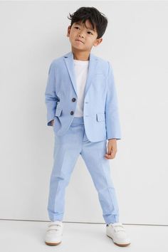 a young boy wearing a blue suit and white shoes standing in front of a wall