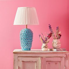 two vases with flowers sit on top of a dresser next to a pink wall