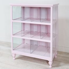 a pink bookcase with glass shelves on the top and bottom, against a white wall