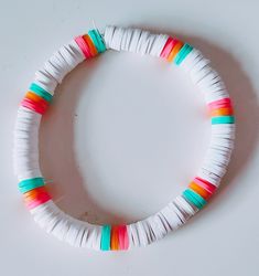 a white bracelet with multicolored paper strips on it's end and an orange bead in the middle