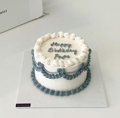 a white and blue birthday cake sitting on top of a table next to a box