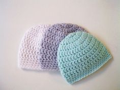 three crocheted hats sitting next to each other on a white surface with one blue and the other green