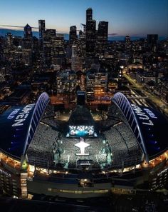 an aerial view of a stadium at night with the city lights lit up in the background