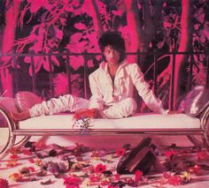 a man sitting on top of a bed surrounded by flowers and other things in front of him