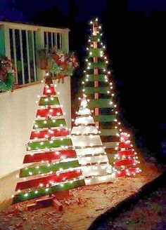 lighted christmas trees on the side of a house in front of a window at night