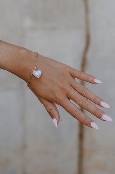 The hand of a model is shown with the Gia Heart Bracelet clasped on her wrist. Heart Bracelet, Paper Clip, A Heart, Heart Charm, Statement Pieces, Timeless Elegance, Natural Beauty, Jewelry Collection, Twist