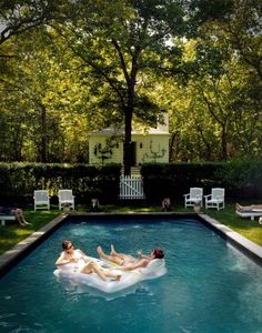 two people floating on inflatable mattresses in a pool surrounded by lawn chairs