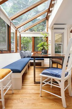 a sun room with wooden floors and white walls, blue cushioned seat covers on the bench