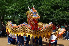 people standing around a dragon statue in the middle of a park