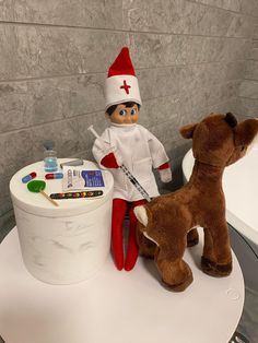 an elf is sitting on top of a table next to a stuffed bear and toy