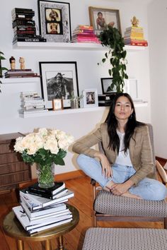 a woman sitting on a chair in a living room next to a table with flowers