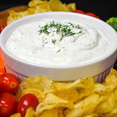 a bowl of dip surrounded by chips, tomatoes and broccoli