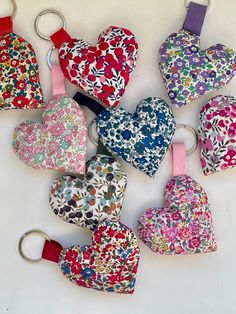 six heart shaped keychains are arranged on a white surface with pink, blue, green, and red flowers