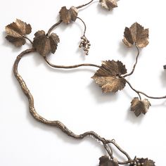 a metal vine with leaves and berries hanging from it's side on a white surface