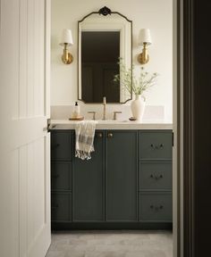 a bathroom with green cabinetry and white counter tops, along with a gold framed mirror above the sink