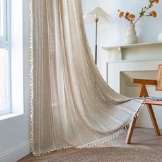 a room with a white curtain and some flowers on the window sill next to a chair