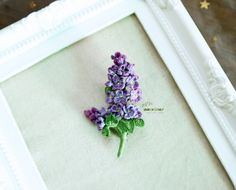 a small purple flower is placed in a white frame on a table next to a star