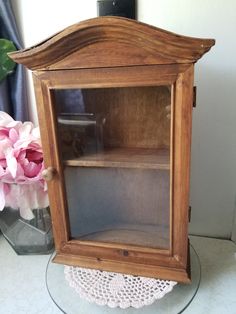 a wooden display case sitting on top of a glass table next to a pink flower