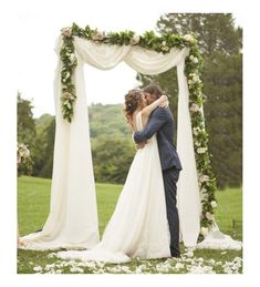 a bride and groom kissing in front of an outdoor wedding ceremony arch decorated with greenery