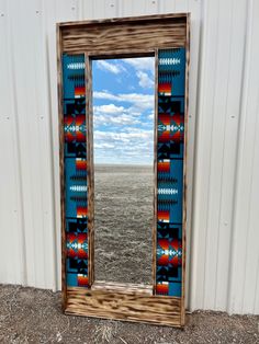 a mirror sitting on the side of a building next to a dirt field in front of a white wall