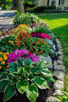 colorful flowers are growing on the side of a rock garden bed in front of a house