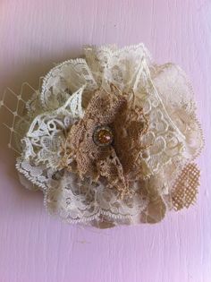 a close up of a lace and fabric flower on a pink surface with white crochet