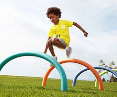 a young boy is jumping over an obstacle made out of colored plastic rings on the grass