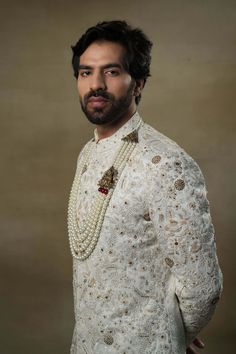 Editor's Note Featuring our work of art in our white all over hand-embroidered sherwani set. The foundation is crafted using machine embroidery adorned with tone on tone thread serving as the base texture, while the second tier showcases highlighting with 3D brass elements, dabka and zari threads. Fabric: Linen silk Color: Ivory, gold Components: Sherwani, kurta and churidar Occasion: Groom Fit: Regular Note: Product colour may slightly vary due to photographic lighting sources Care: Dry clean o Off White Naqshi Traditional Wear For Festive Occasions, Off White Bandhgala With Naqshi For Festive Occasions, Off White Naqshi Bandhgala For Festive Occasions, Designer Festive Sets With Chikankari Embroidery, Designer Off White Traditional Wear With Chikankari Embroidery, Designer Resham Embroidery Kurta For Traditional Ceremonies, Gold Chikankari Embroidery Sets For Reception, Gold Sets With Chikankari Embroidery For Reception, Designer Traditional Wear With Chikankari Embroidery For Ceremonies